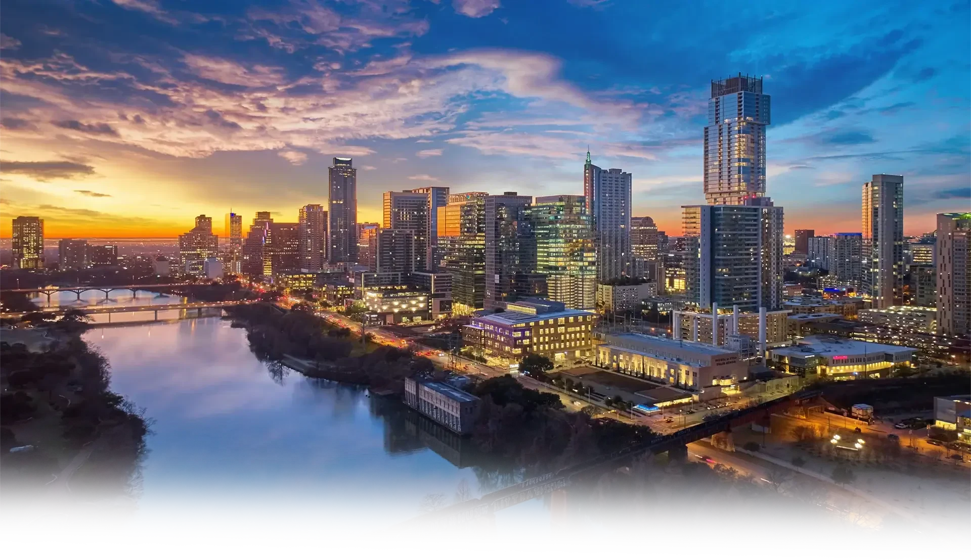 Austin, Texas skyline at sunset with the Colorado River and downtown high-rise buildings.