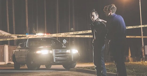 Police officers investigating a nighttime crime scene with a patrol car and police tape